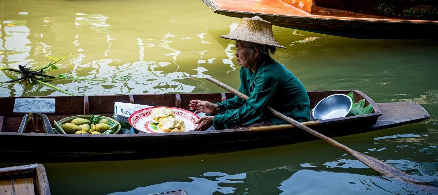 Femme qui vend des fruits sur un bateau, au marché flottant d'Amphawa